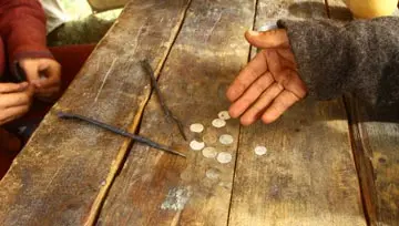 Hand in tattered sleeve showing coins on an old wood table