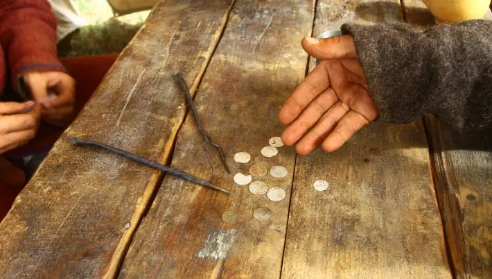 Hand in tattered sleeve showing coins on an old wood table