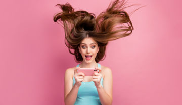 young woman playing Grande Vegas on her phone and her hair is blown away by her excitement