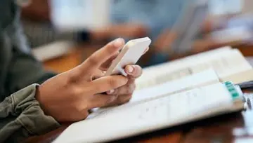 scrolling through a phone while looking in a book 