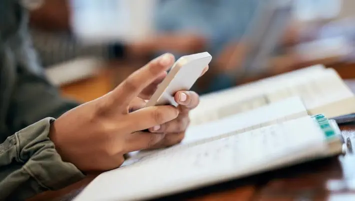 scrolling through a phone while looking in a book 