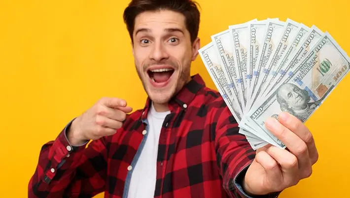 a man happily showing us his handful of $100 bills on a yellow background