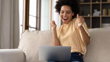woman on a laptop cheering her win on Grande Vegas Casino