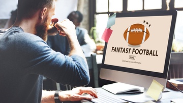 man sitting at his computer looking at fantasy football on his screen